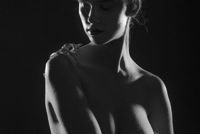 Close-up of shirtless woman with skeleton hand on shoulder against black background