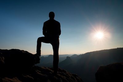 Silhouette man on rock against sky