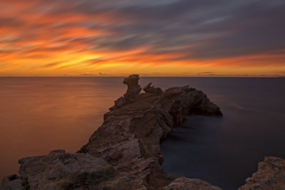 Rock formation on beach against sky during sunset