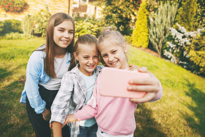 Group of happy teenage girls laughing and taking a selfie on a mobile phone outdoors.