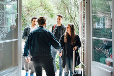 Rear view of owner handshaking with guests while standing in doorway