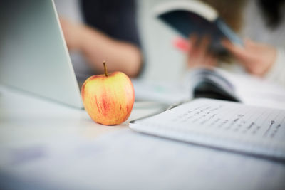 Close-up of apple by laptop and book on table in university