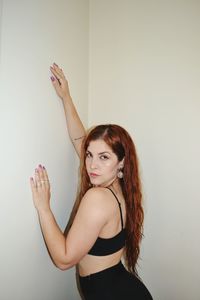 Portrait of young woman with arms raised against wall
