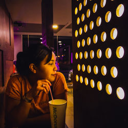 Woman looking away while sitting at illuminated shop