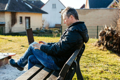 Man working on laptop outdoors, sitting playground. concept of remote work of parents with children