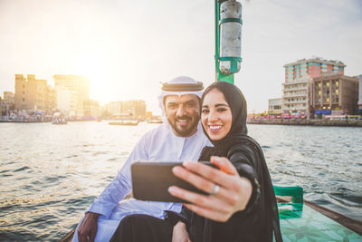 Couple talking selfie while sitting in boat on river during sunset