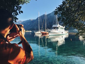 Rear view of man photographing boat on river