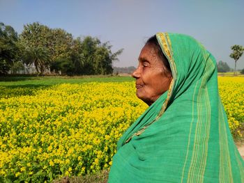 Portrait of woman standing amidst yellow flowering plants on field