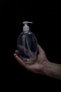 Person holding glass bottle against black background
