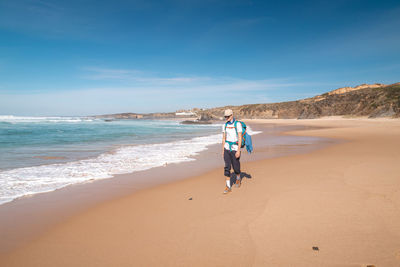 Rear view of woman walking at beach against sky