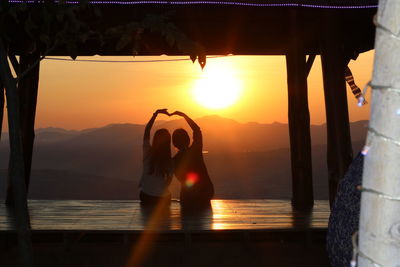 Rear view of friends making heart shape against sky during sunset
