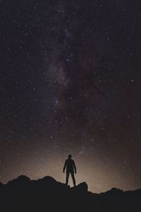 Silhouette man standing on rock formation against milky way