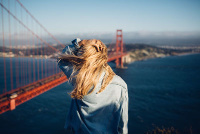 Rear view of woman standing by suspension bridge against sky