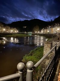 Illuminated railing by river against sky at night