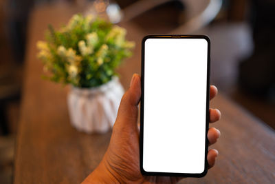 Close-up of hand holding mobile phone on table