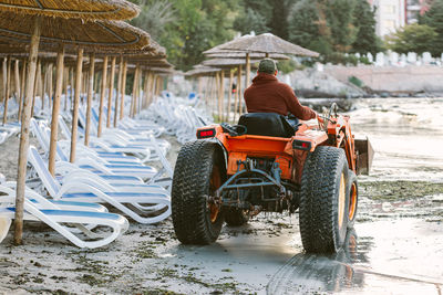 Tractor cleaning a beach with lounge chairs and straw umbrellas at sunrise
