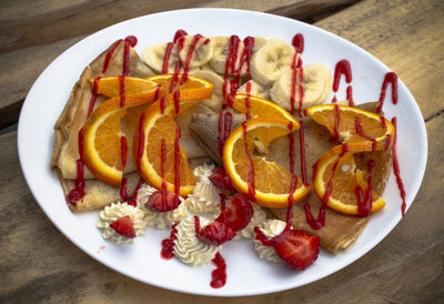 Pancakes with cranberry jam, strawberries, bananas, cream, and strawberry topping.