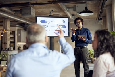 Businessman gesturing at male colleague with hand raised during meeting in office