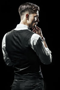 Rear view of young man standing against black background