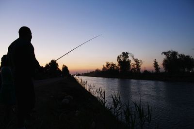 Silhouette father with daughter fishing at river