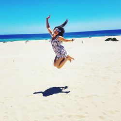 Full length of young woman jumping on sand against sea at beach