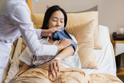 Nurse taking mature female patient blood pressure in hospital bed