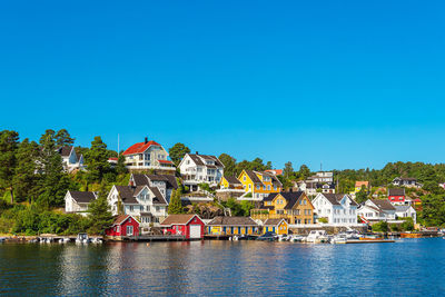 Buildings by river against clear blue sky