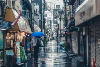 Person walking on wet street during rainy day holding a blue umbrella