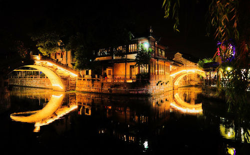 Illuminated city by river against sky at night