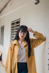 Portrait of young woman standing against wall