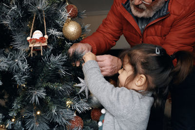 Grandparents decorate the christmas tree with their little granddaughter