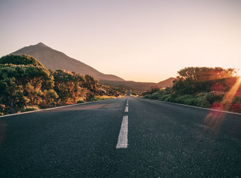 Road leading towards mountains against clear sky