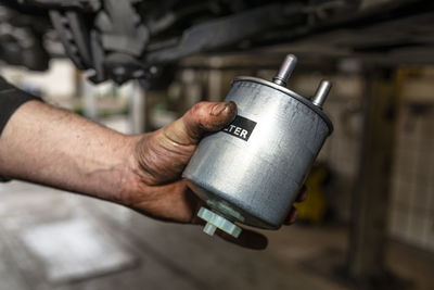 Car mechanic holding in hand a new fuel filter, in the background car on a lift in a car workshop.