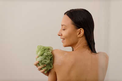 Side view of young woman holding flower against wall