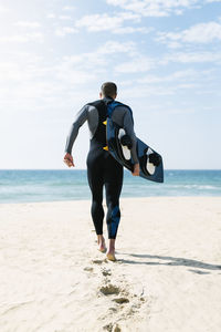 Rear view of man standing on beach against sky