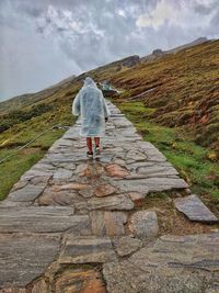 Rear view of man walking on footpath against sky