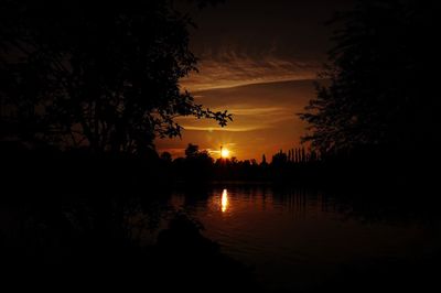 Silhouette trees by lake against sky during sunset