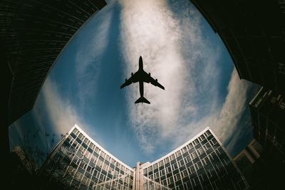 Low angle view of airplane flying over buildings in sky