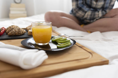 Close up of women's legs and a breakfast tray with fruits on a bed.