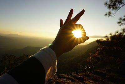 Close-up of hand holding sun during sunset