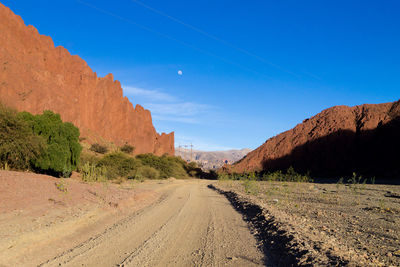 Dirt road leading towards mountains against blue sky