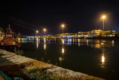 Illuminated city by river against sky at night