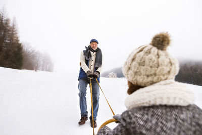 Happy senior couple having fun with sledge in snow-covered landscape