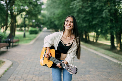 A cheerful musician girl enjoys playing the guitar in the park and laughs. music, musician, guitar