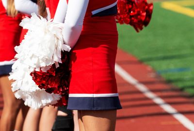 A high school cheerleader holding pom poms behind her back.