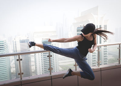 Woman jumping by railing against buildings