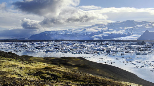 Scenic view of sea by snowcapped mountains against sky