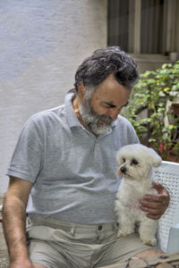 A man is playing with his little maltese dog. 