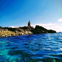 Lighthouse by sea against blue sky