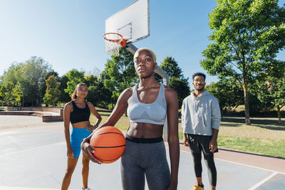 Confident friends with ball in basketball court on sunny day